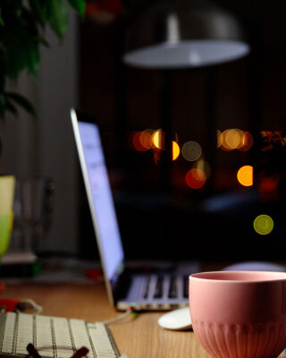 Comfortable workspace for distance job at home - mug of tea, computer, laptop, lamp, digital tablet, smartphone, houseplant, notebook, armchair. Selective focus on mug.